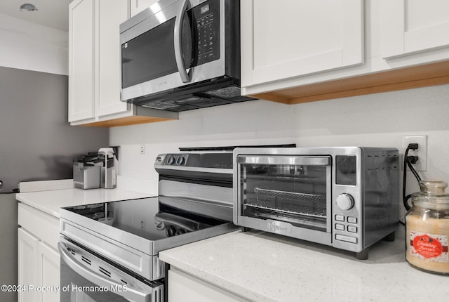 kitchen with light stone counters, white cabinetry, and appliances with stainless steel finishes