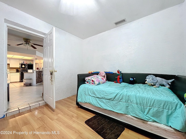 bedroom with ceiling fan, black fridge, and light wood-type flooring