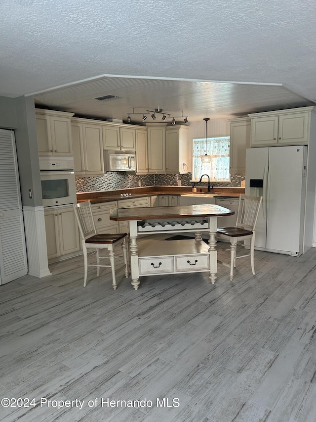 kitchen featuring sink, light hardwood / wood-style flooring, a textured ceiling, decorative light fixtures, and white appliances