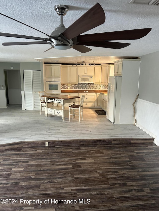 kitchen with hardwood / wood-style floors, white appliances, tasteful backsplash, and a textured ceiling