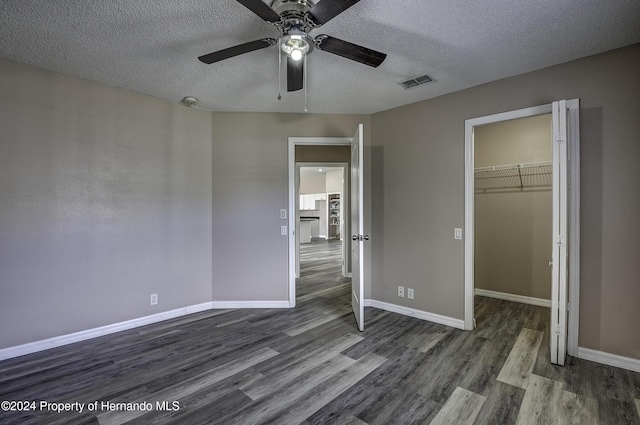 unfurnished bedroom with a walk in closet, a textured ceiling, ceiling fan, dark wood-type flooring, and a closet