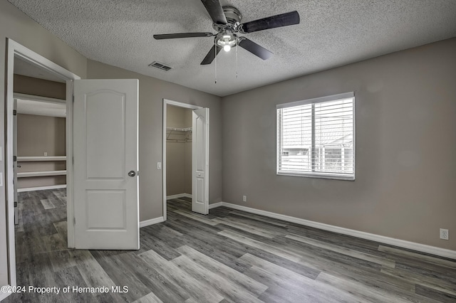 unfurnished bedroom featuring light hardwood / wood-style flooring, ceiling fan, a spacious closet, a textured ceiling, and a closet