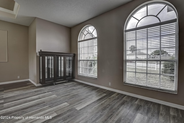 empty room with a textured ceiling, baseboards, and wood finished floors