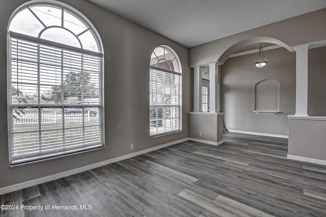 unfurnished room with a healthy amount of sunlight, ornate columns, a textured ceiling, and wood finished floors