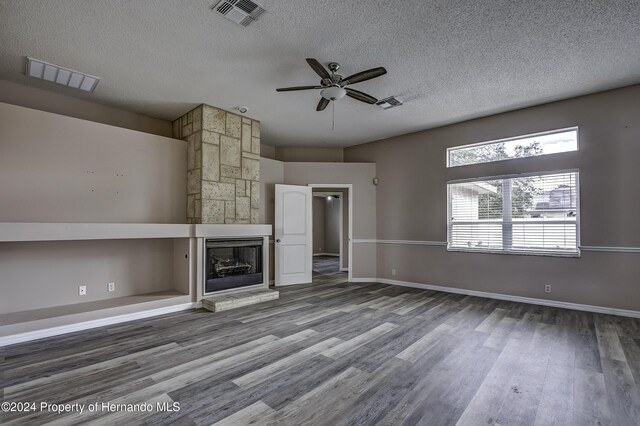 unfurnished living room with visible vents, a stone fireplace, a textured ceiling, and wood finished floors