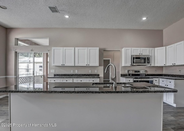 kitchen with stainless steel appliances, dark stone countertops, a sink, and white cabinets