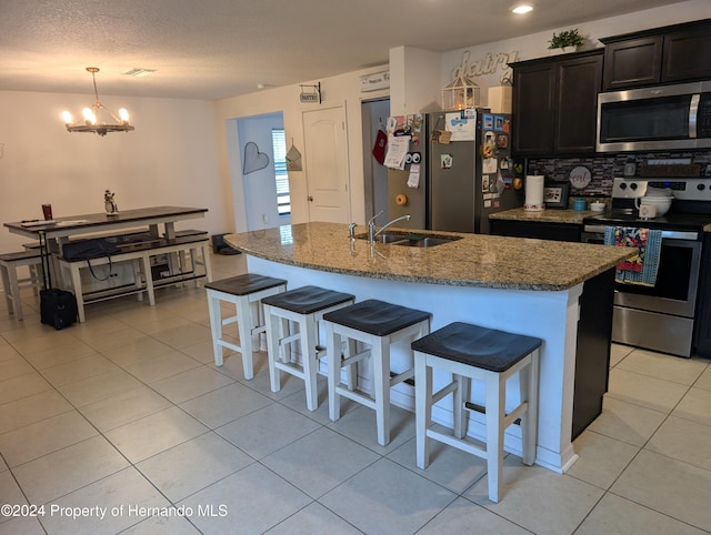 kitchen featuring backsplash, sink, an island with sink, appliances with stainless steel finishes, and light stone counters