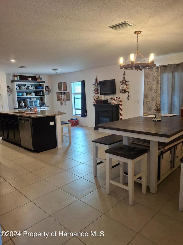 kitchen with hanging light fixtures, stainless steel dishwasher, a textured ceiling, a breakfast bar area, and light tile patterned floors