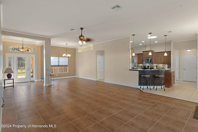 unfurnished living room featuring tile patterned floors, crown molding, and ceiling fan with notable chandelier