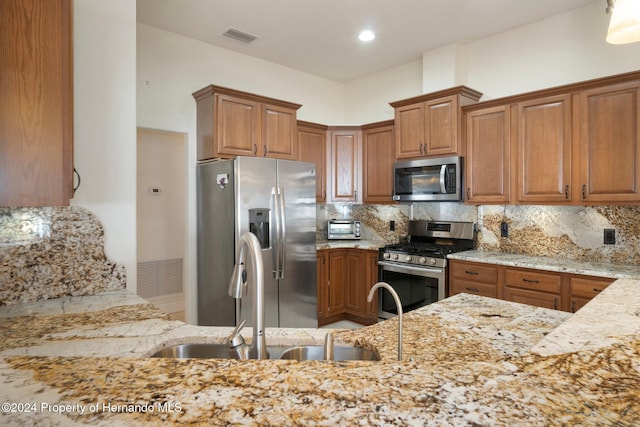 kitchen with sink, appliances with stainless steel finishes, tasteful backsplash, light stone counters, and kitchen peninsula