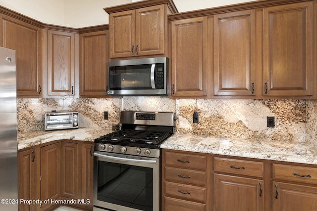 kitchen with decorative backsplash, light stone countertops, and appliances with stainless steel finishes