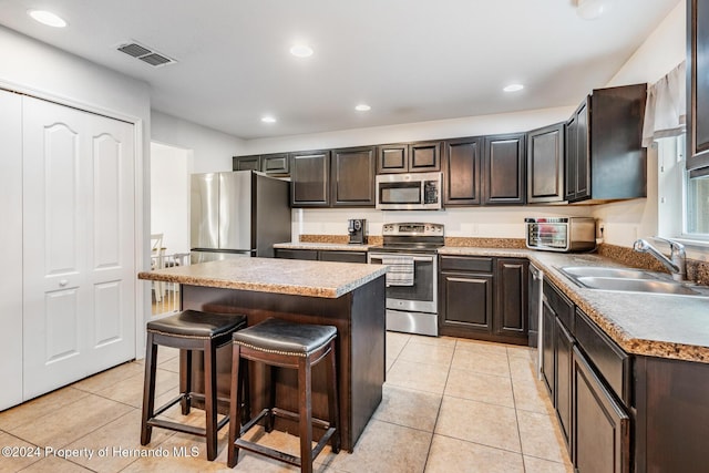 kitchen featuring light tile patterned flooring, sink, appliances with stainless steel finishes, a kitchen island, and a breakfast bar area