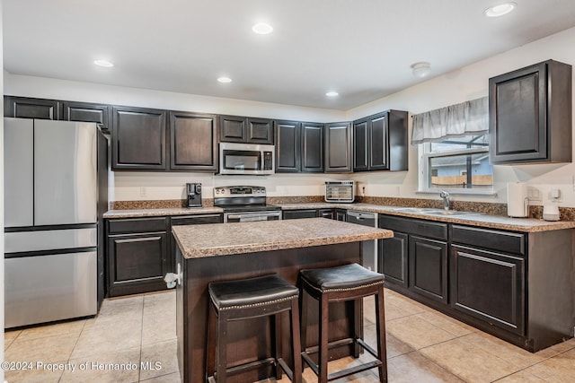 kitchen with appliances with stainless steel finishes, sink, light tile patterned floors, a center island, and a breakfast bar area