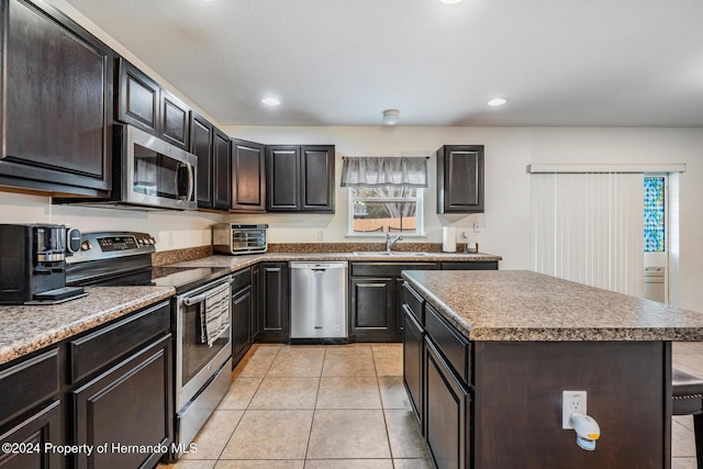 kitchen with a breakfast bar, stainless steel appliances, sink, a center island, and light tile patterned flooring