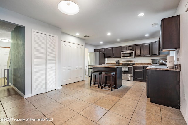 kitchen featuring a center island, stainless steel appliances, a breakfast bar, light tile patterned flooring, and dark brown cabinets