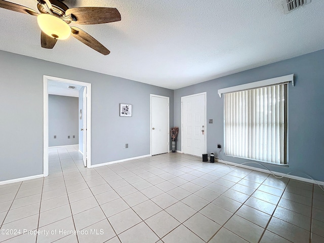 empty room featuring ceiling fan, light tile patterned floors, and a textured ceiling