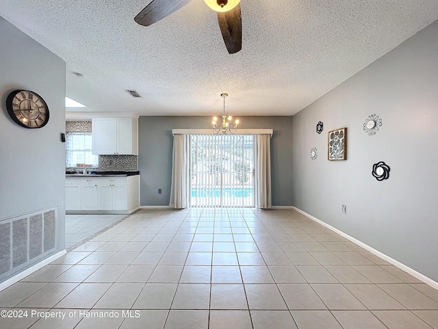 unfurnished dining area featuring ceiling fan with notable chandelier, sink, light tile patterned floors, and a textured ceiling