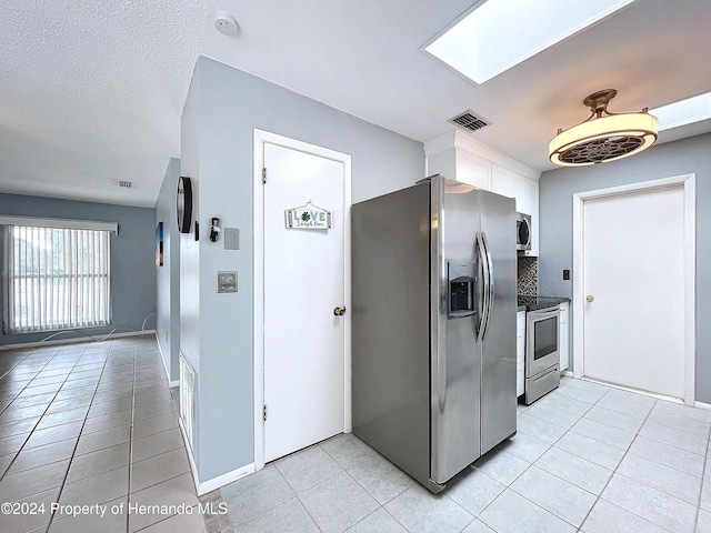 kitchen featuring a skylight, decorative backsplash, light tile patterned floors, a textured ceiling, and stainless steel appliances