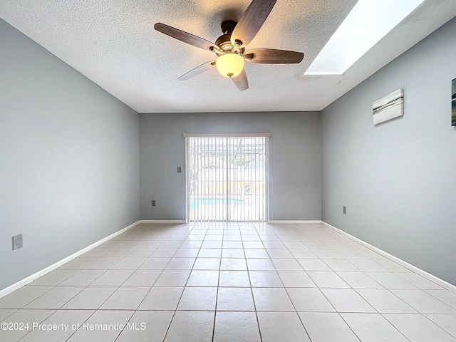 empty room featuring a skylight, ceiling fan, light tile patterned flooring, and a textured ceiling