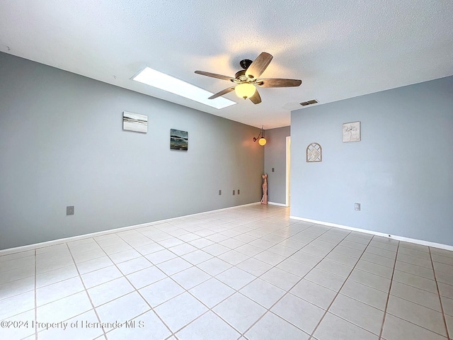 tiled spare room featuring a skylight, ceiling fan, and a textured ceiling