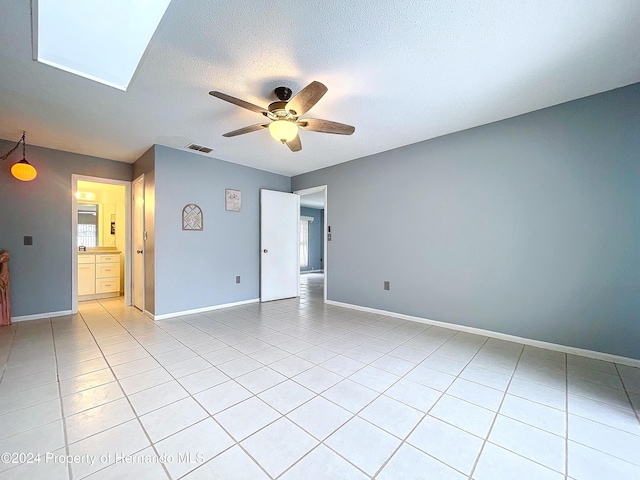 empty room featuring light tile patterned floors, a textured ceiling, a skylight, and ceiling fan