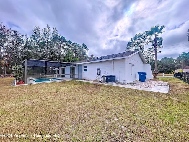 rear view of property featuring a yard, a lanai, cooling unit, a fenced in pool, and a patio