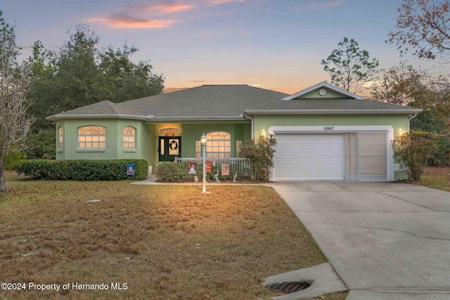 ranch-style home featuring a yard, a porch, and a garage