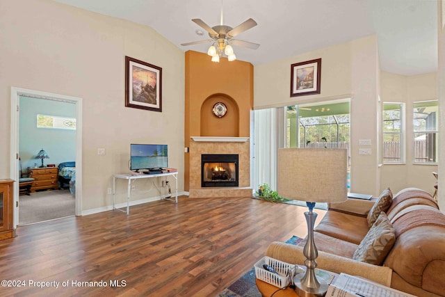 living room with hardwood / wood-style floors, ceiling fan, a towering ceiling, and a tiled fireplace