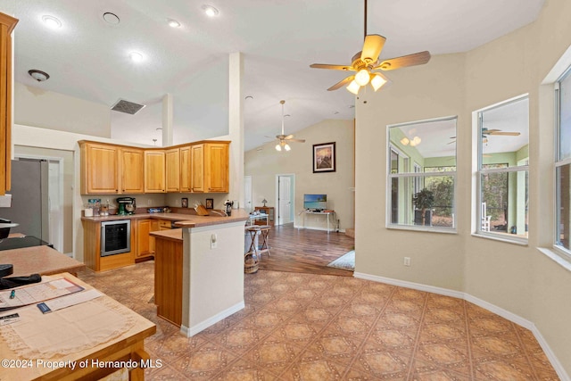 kitchen featuring high vaulted ceiling, wine cooler, kitchen peninsula, a breakfast bar area, and stainless steel refrigerator