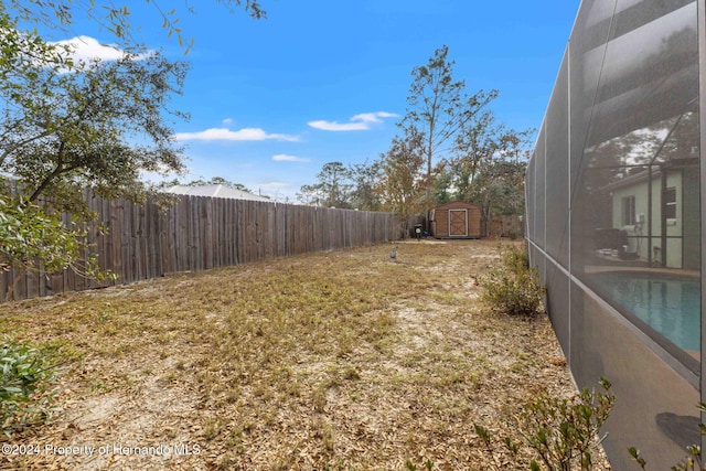 view of yard with a fenced in pool, glass enclosure, and a storage shed