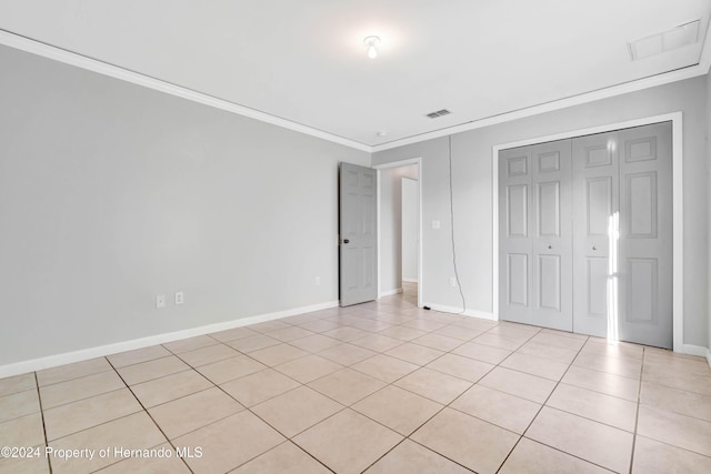 unfurnished bedroom featuring light tile patterned floors, crown molding, and a closet