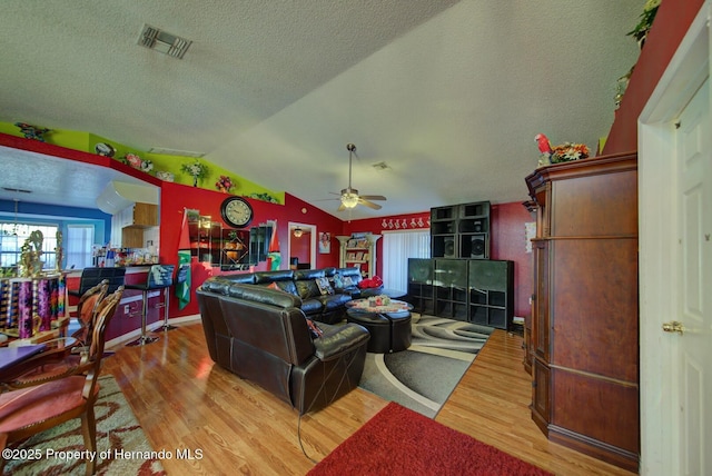 living room with a textured ceiling, light wood-type flooring, vaulted ceiling, and ceiling fan