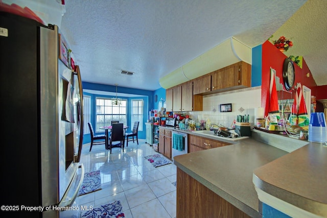 kitchen with sink, backsplash, a textured ceiling, light tile patterned flooring, and appliances with stainless steel finishes