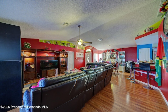 living room featuring a textured ceiling, ceiling fan, wood-type flooring, and lofted ceiling