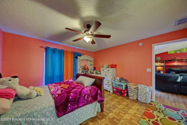 bedroom with ceiling fan, light parquet floors, and a textured ceiling