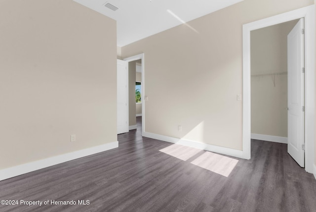 unfurnished bedroom featuring dark hardwood / wood-style flooring, a walk in closet, and a closet