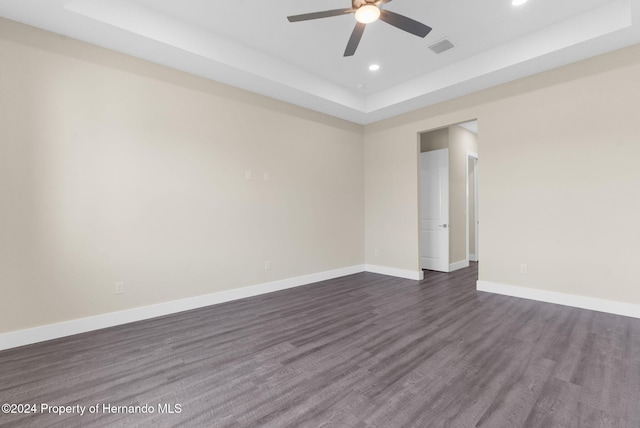 unfurnished room featuring a tray ceiling, ceiling fan, and dark wood-type flooring