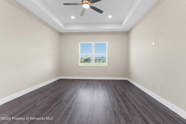 unfurnished room featuring a tray ceiling, ceiling fan, and dark wood-type flooring