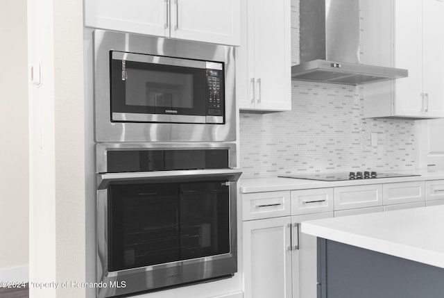 kitchen featuring decorative backsplash, stainless steel appliances, white cabinets, and wall chimney exhaust hood