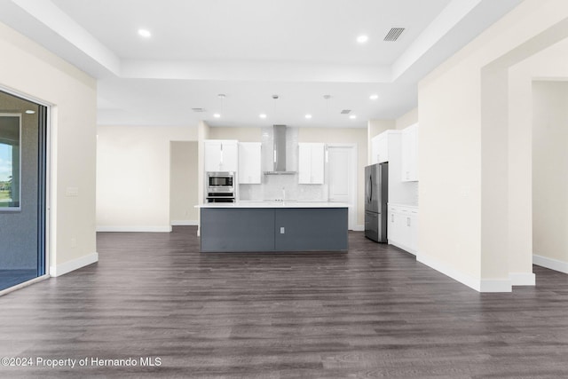 kitchen featuring wall chimney exhaust hood, white cabinetry, an island with sink, and appliances with stainless steel finishes