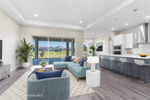 living room with a chandelier, light hardwood / wood-style floors, a raised ceiling, and sink