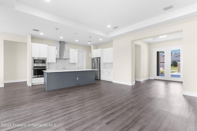 kitchen featuring white cabinets, an island with sink, stainless steel appliances, and wall chimney range hood