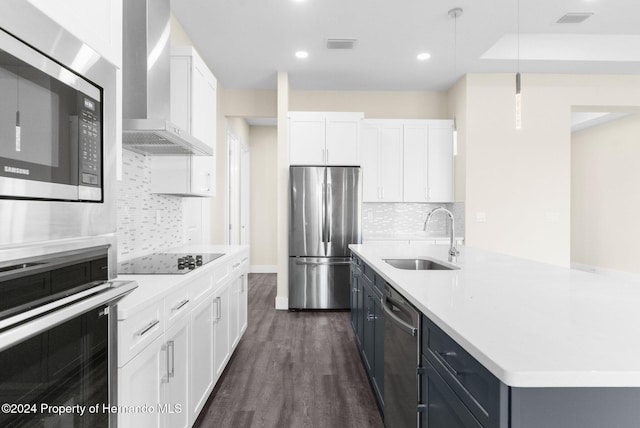 kitchen featuring stainless steel appliances, wall chimney range hood, sink, decorative light fixtures, and white cabinetry