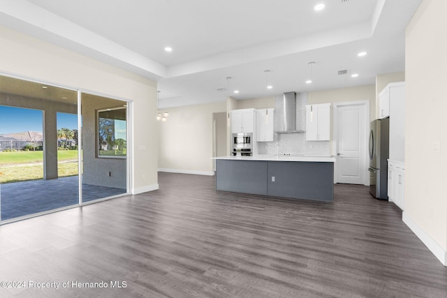 kitchen with wall chimney exhaust hood, dark hardwood / wood-style flooring, a kitchen island with sink, white cabinets, and appliances with stainless steel finishes