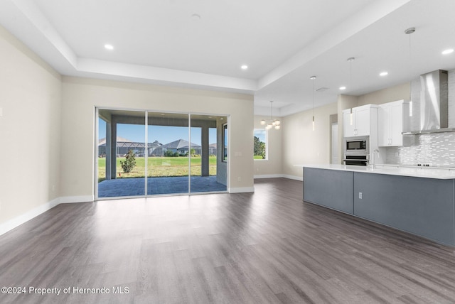 unfurnished living room featuring a notable chandelier, dark hardwood / wood-style floors, sink, and a tray ceiling