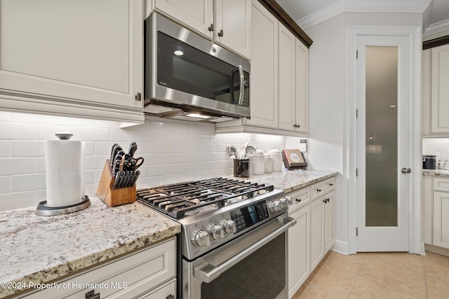 kitchen with light stone countertops, stainless steel appliances, backsplash, light tile patterned flooring, and ornamental molding