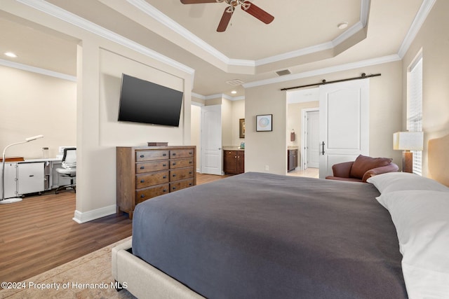 bedroom with a raised ceiling, ceiling fan, a barn door, light hardwood / wood-style flooring, and connected bathroom