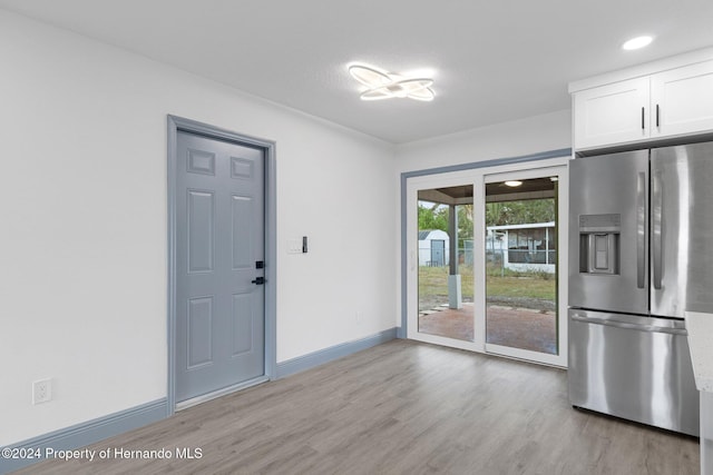 interior space with light hardwood / wood-style floors, stainless steel fridge, and white cabinetry