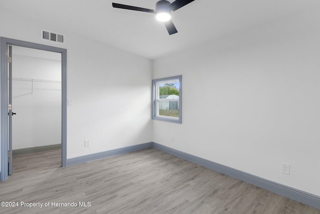 unfurnished bedroom featuring a walk in closet, ceiling fan, a closet, and light hardwood / wood-style flooring