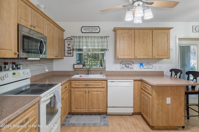 kitchen with ceiling fan, sink, kitchen peninsula, white appliances, and a breakfast bar